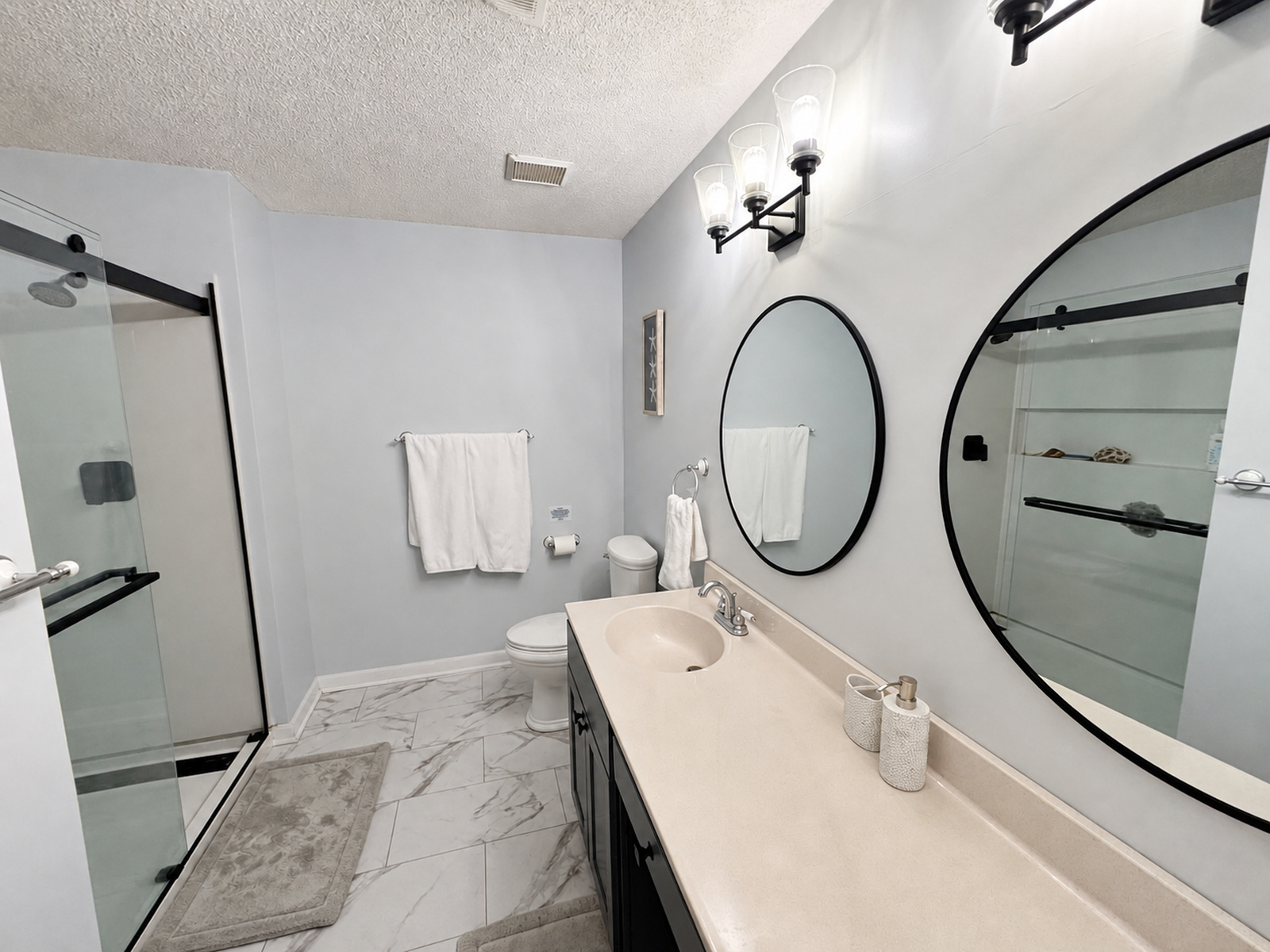 En suite bathroom at Beaches Be Salty with round mirror, vanity, and walk-in glass shower
