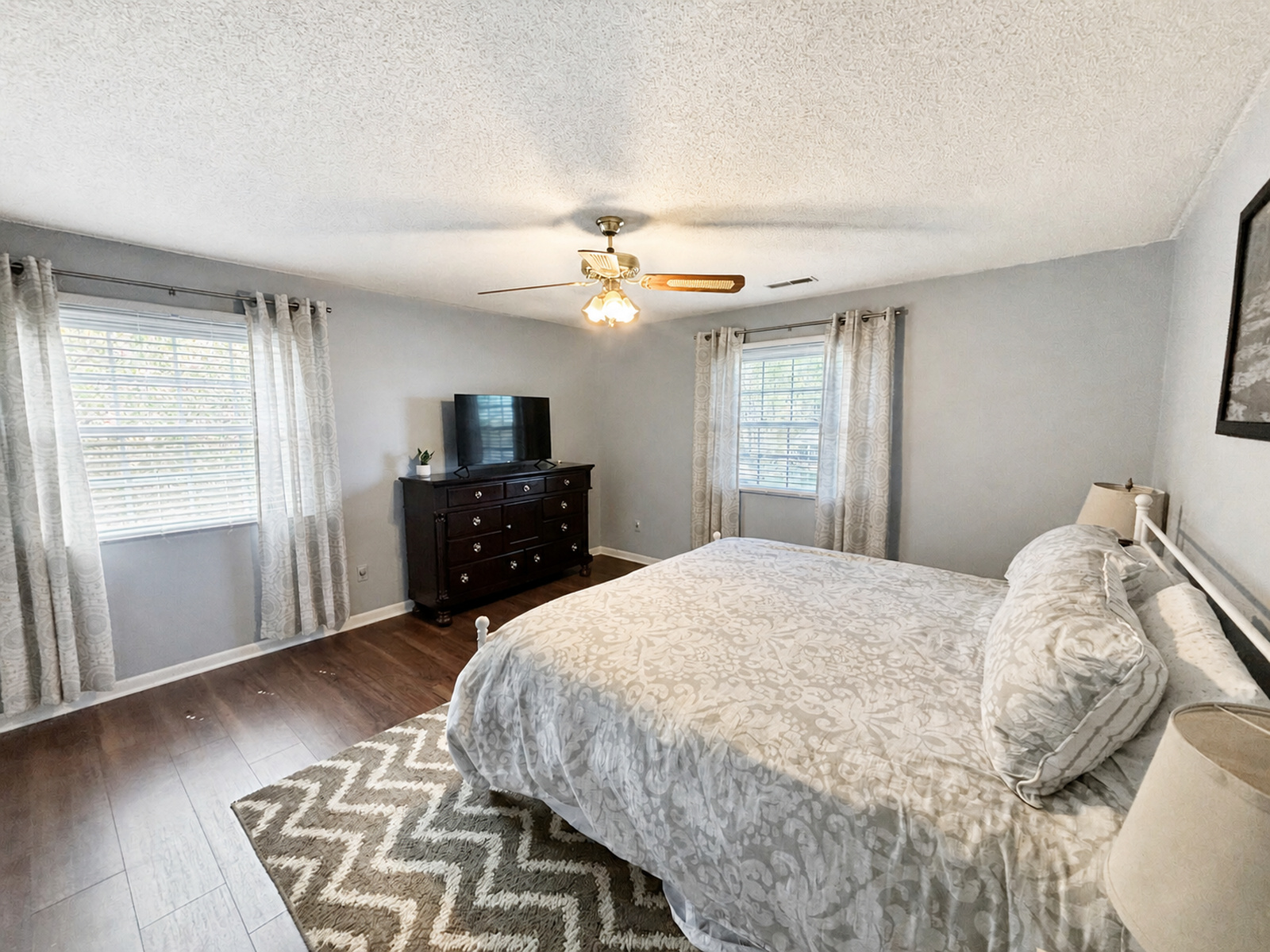 Guest bedroom at Beaches Be Salty with patterned bedspread, ceiling fan, TV, and two windows