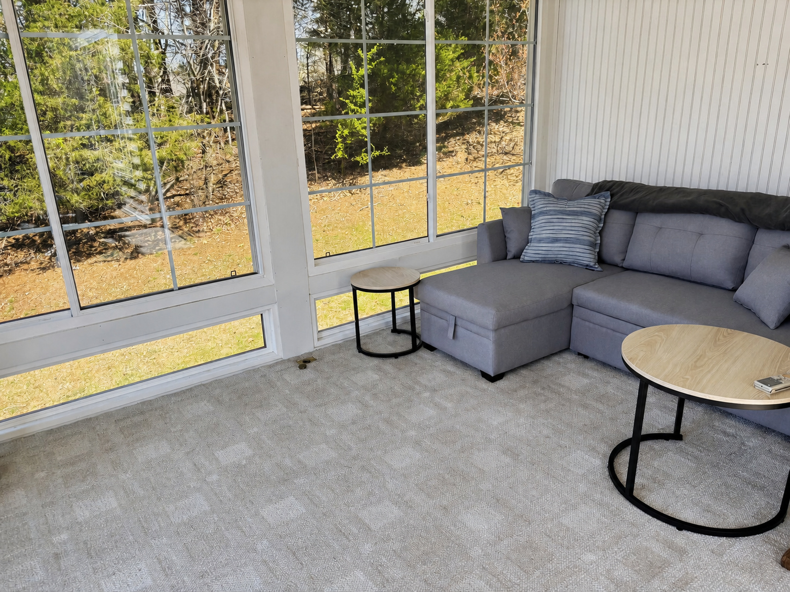 Window-lined sunporch at Beaches Be Salty with a sectional sofa and wooded view